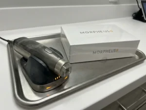 Gebruikte Morpheus8 radiofrequentie microneedling handstuk op klinische tray naast verzegelde nieuwe verpakking, zichtbaar stoflaagje op oud apparaat.