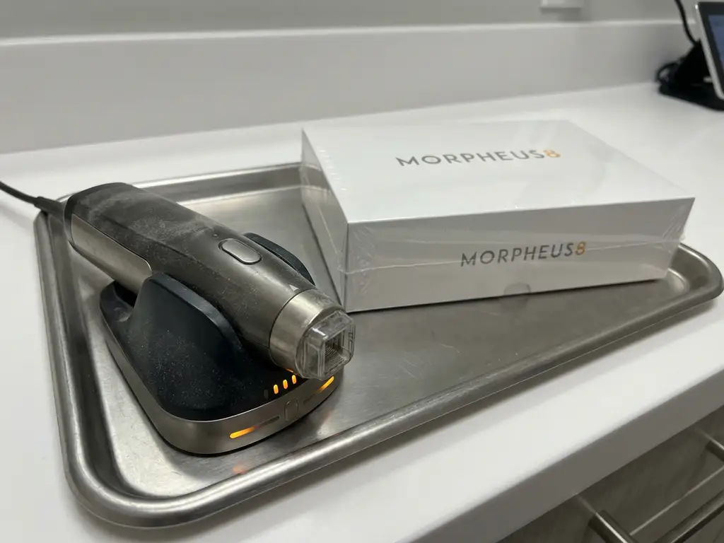 Gebruikte Morpheus8 radiofrequentie microneedling handstuk op klinische tray naast verzegelde nieuwe verpakking, zichtbaar stoflaagje op oud apparaat.