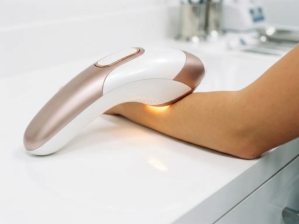 IPL-apparaat met warm lichtpuls op onderarm, glanzend wit met rosé goud afwerking op klinisch witte ondergrond.