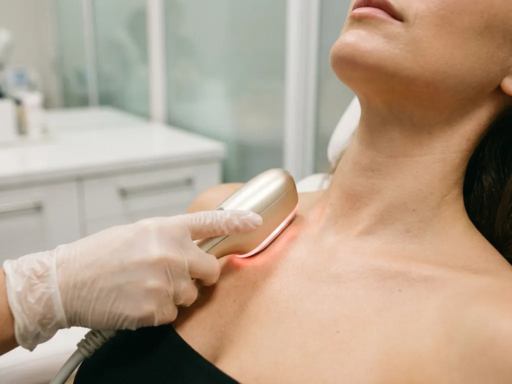Vrouwenhals en décolleté tijdens een medisch-esthetische behandeling met een strak apparaat, stralende huid in zachte klinische omgeving.